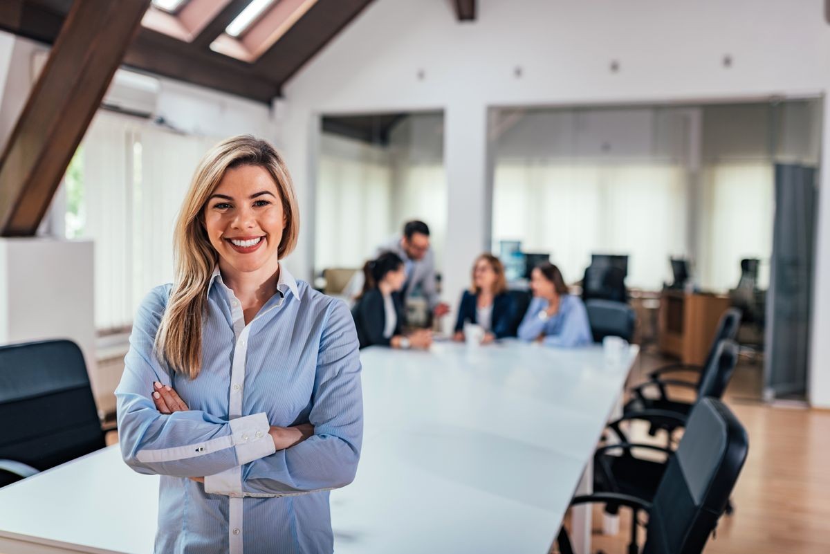 Portrait of a smiling female business leader. Colleagues in the background.